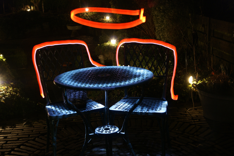 AC01.jpg - Hier is er met het licht van een zaklantaarn een lichtrand langs de stoelen en een cirkel boven de tafel gemaakt. Dit zorgt ook voor het licht op het tuinsetje. Mooi effect. Vooral omdat de tuin ook nog een beetje verlicht is.