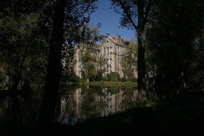 AF02.jpg - Ondanks de hele donkere omgeving is het gebouw en het spiegelbeeld in het water goed belicht. Persoonlijk denk ik dat ik ook bij deze foto zou hebben gekozen voor een staande uitsnede waarbij het beeld links en rechts zou worden begrensd door de twee bomen. Het grote donkere deel maakt het beeld van de foto wat te donker.