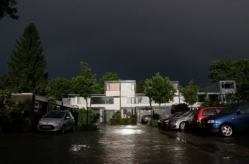 AC01.jpg - Een hele mooie foto die huizen en straat verlicht door de zon en dan die inktzwarte onweerslucht er achter. Belichting, scherpte alles samen geeft de sfeer perfect weer.